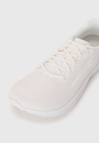 Baskets de course blanches en mesh respirant avec des lacets blancs, un col rembourré et un logo discret sur un fond blanc.