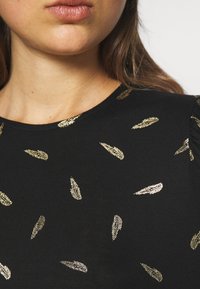 Schwarzes Oberteil mit rundem Ausschnitt, das mit verstreuten, metallischen Goldblättern verziert ist. Glatte Textur mit kurzen, gerafften Ärmeln.