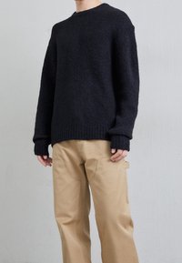 Gruboszyty czarny sweter z prążkowanymi mankietami i dołem, w połączeniu z beżowymi spodniami z bocznymi kieszeniami i dekoracyjnymi detalami szycia.