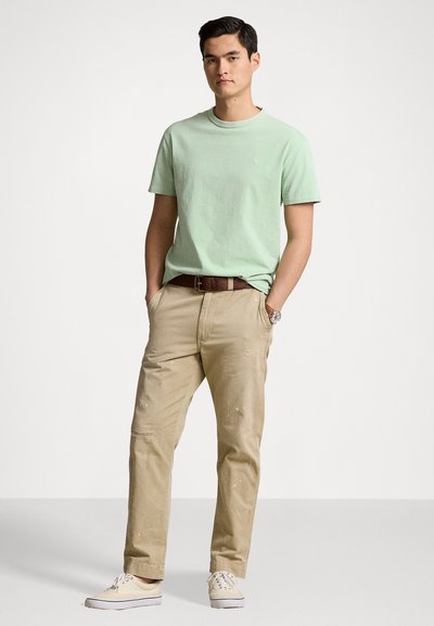 Ljusgrön bomullströja, khaki canvasbyxor med slitna detaljer, brun läderbälte och beige sneakers med vita snören.