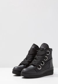 Zapatillas altas negras con acabado de cuero texturizado, con ojales sobredimensionados, cordones gruesos negros y un tobillo acolchado.