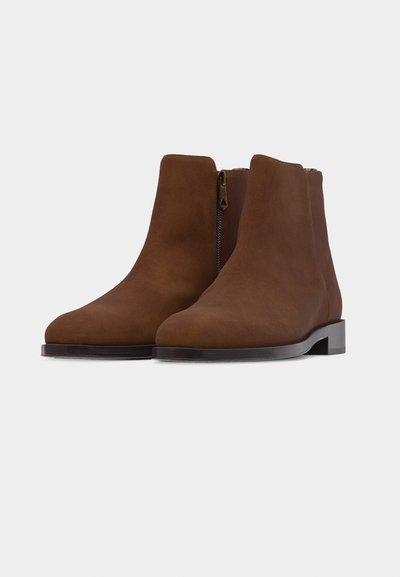 Paire de bottines en daim marron avec fermetures éclair latérales, talons bas et bouts arrondis, présentées sur un fond blanc uni.