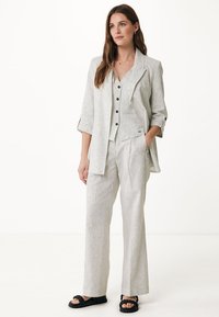 Pasiasty garnitur trzyczęściowy w jasnoszarym i białym kolorze, składający się z dopasowanej marynarki, zapiętej kamizelki oraz spodni z szerokimi nogawkami, zestawiony z czarnymi sandałami.