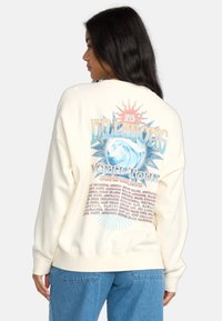 Crème-kleurige sweatshirt met een grafisch ontwerp op de achterkant met een zonnestraalontwerp, tekst en golfillustratie. Zacht stof, relaxed fit.