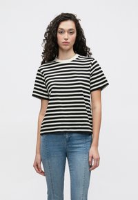 Črno-bela črtasta majica s pilčastim izrezom in kratkimi rokavi, narejena iz mehke bombažne tkanine, kombinirana z modrimi denim hlačami.