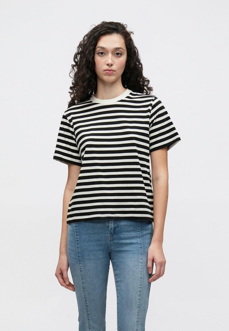 Črno-bela črtasta majica s pilčastim izrezom in kratkimi rokavi, narejena iz mehke bombažne tkanine, kombinirana z modrimi denim hlačami.