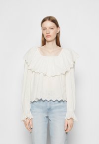 Blusa branca com design de camadas de volantes, bainha com bordas onduladas e bordado de print floral. Mangas longas e ajustadas com punhos em volantes.