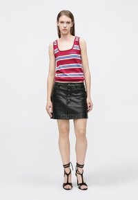 Camiseta sin mangas con rayas rojas y azules y tirantes anchos, combinada con una minifalda de cuero negra con botones al frente y textura suave. Tacones negros con tiras.