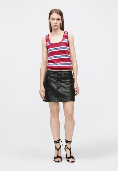 Camiseta sin mangas con rayas rojas y azules y tirantes anchos, combinada con una minifalda de cuero negra con botones al frente y textura suave. Tacones negros con tiras.