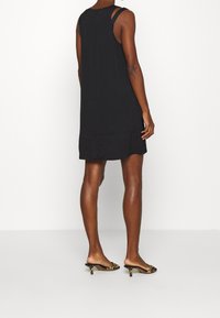 Vestido negro sin mangas con un corte relajado, que presenta un diseño en capas y un escote en la espalda. Se lleva con tacones de punta abierta con estampado de leopardo.