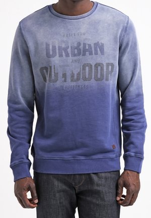 Mand iført en blå ombre langærmet sweatshirt med teksten "Urban and Outdoor" trykt på fronten.