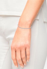 Bracciale d'argento con un motivo alternato di piccole pietre trasparenti incastonate in una delicata catena, indossato su un polso con smalto per unghie di colore chiaro.