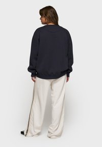Felpa grigia scura con maniche larghe, polsini e orlo a coste. Abbinata a pantaloni color crema con una striscia laterale nera e beige.