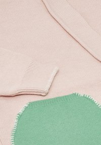 Könnyű rózsaszín kötött pulóver zöld folttal. Bordázott mandzsettákkal és kontrasztos fehér varrással a zöld rész szélein.