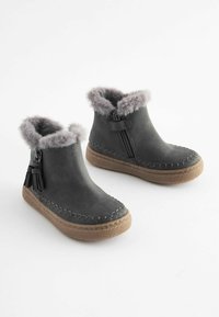 Stivaletti in suede grigi con fodera in pelliccia sintetica, suola in gomma marrone texturizzata, cuciture decorative e zip laterale per una facile calzata.