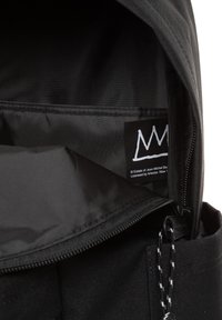 Interior de mochila negra con una textura de nailon suave, cierre con cremallera y una etiqueta con un logo de corona blanca sobre un fondo negro.