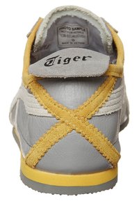 Šedé kožené tenisky s žlutými semišovými akcenty a X-ovými designy na patě. Mají polstrovaný límec a logo značky na jazyku.