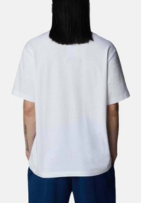 T-shirt bianco in cotone con una vestibilità rilassata, maniche corte e orlo dritto, visto da dietro. Design semplice, nessun motivo visibile.