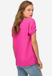 Blusa corta a maniche corte di colore rosa brillante con scollatura rotonda e maniche arrotolate. Tessuto morbido con una vestibilità rilassata, abbinata a jeans di denim blu chiaro.