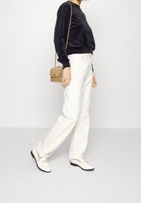Sammetsblå sweatshirt, vita högmidjade jeans och vita loafers med svarta sulor. Liten beige crossbody-väska med kedjestropp.
