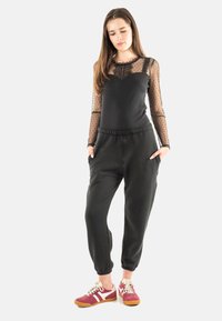 Top negro de manga larga con mangas de tul con lunares, combinado con pantalones jogger negros. La modelo lleva zapatillas rojas y blancas.