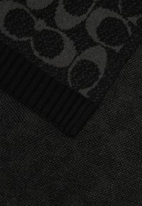 Melnās tekstila audums ar teksturētu rakstu, kas sastāv no aplīšiem. Apakšējā mala ir ribota, kas veicina kopējo tumšo izskatu.