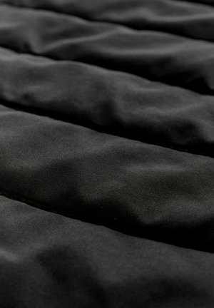 Juodas paminkštintas audinys su lygiu paviršiumi, kuriame yra siuvinėti vertikalūs kanalai, formuojantys siuvinėtą raštą. Vienoda spalva visame paviršiuje.