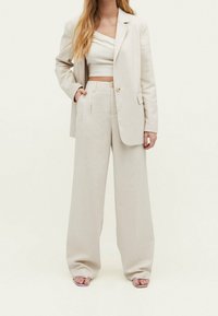 Beige linnen pak met een dubbel-breasted blazer en wijde broek, gecombineerd met een strakke crop top en open teensandalen.
