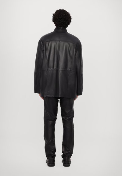 Chaqueta de cuero negra con un ajuste relajado, que presenta una textura suave y un diseño minimalista; combinada con pantalones de cuero negro a juego y botas.