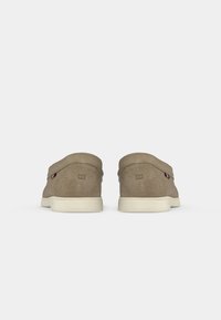 Brown suede shoes with a smooth texture, featuring a simple design, white soles, and small logo accents on the sides.