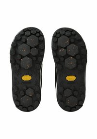 Suela Vibram en negro con tracción hexagonal y circular. Superficie texturada con motas naranjas. Marca dorada en el talón.