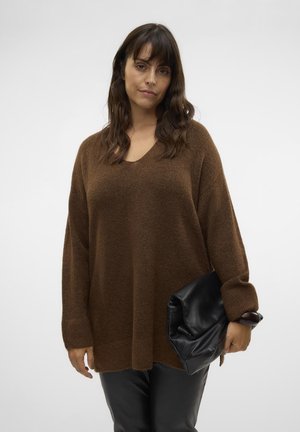 Brown oversized knit sweater with a V-neck and ribbed cuffs, paired with a black fold-over clutch. Model wears fitted black pants.