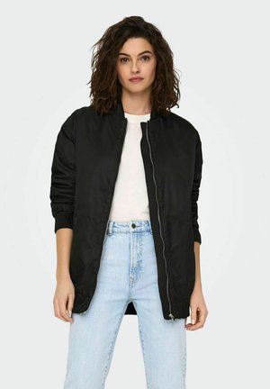 Black bomber jacket with a zip front, ribbed cuffs, and a smooth, shiny texture, paired with a white shirt and light blue jeans.