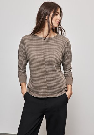 Braun strukturierter Langarm-Top mit rundem Ausschnitt und gemustertem Stoff, kombiniert mit schwarzen Weitbein-Hosen.