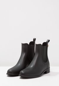 Botas Chelsea de goma negra con superficie lisa, paneles laterales elásticos y tiradores. Tacones bajos para mayor estabilidad.