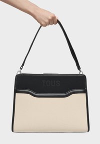 Czarna i beżowa torba na ramię o zwartej konstrukcji, z korpusem z materiału płóciennego, gładkimi skórzanymi akcentami i wytłoczonym logo "TOUS".