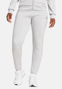 Light gray athletic pants made from smooth fabric, featuring a slim fit. Includes subtle three-stripe logo detail on the left leg.