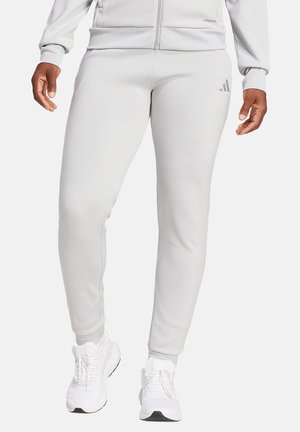 Pantalon de sport gris clair en tissu lisse, avec une coupe slim. Comprend un discret logo à trois bandes sur la jambe gauche.