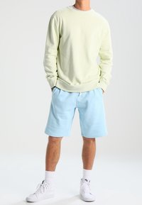 Sweat-shirt jaune clair à col rond, associé à un short bleu clair. Les deux sont en tissu doux, avec une coupe décontractée. Chaussures de sport blanches.