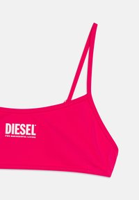 Rosa croppad topp av mjukt tyg, med tunna band och "DIESEL"-logotypen i vitt framtill.