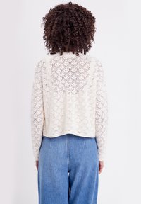 Suéter de punto color crema con un patrón de rombos, diseño corto, mangas largas y dobladillo acanalado, combinado con jeans azul de cintura alta.