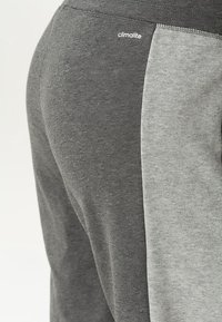 Gros plan d'un pantalon en tissu gris bicolore avec le logo "climalite" sur le côté plus foncé près de la ceinture.