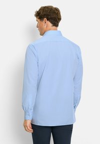 Camicia a maniche lunghe azzurra chiara con colletto a punte, polsini con bottoni e una sottile texture. Il retro presenta una piega per facilitare i movimenti.