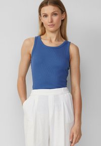 Blauw geribbelde tanktop met een ronde halslijn, gecombineerd met witte wijde broek met plooien en zijzakken. Overal een soepele textuur.