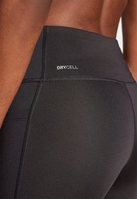 Svarte atletiske leggings med høy midje, glatt tekstur og DRYCELL-merke. Merkbare flate sømmer øker holdbarheten.