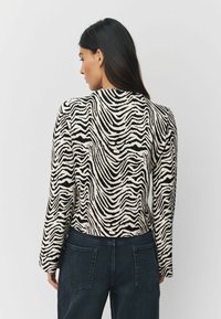 Sveter so zebrovým vzorom v krémovej a čiernej farbe, s dlhými rukávmi a textúrovaným povrchom. Kombinovaný s tmavými džínsami.