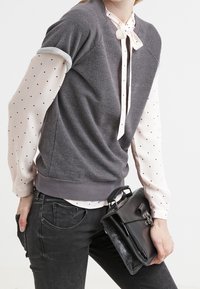 Pull gris à manches courtes porté par-dessus un chemisier rose clair à pois, associé à un jean noir et un sac à main noir.