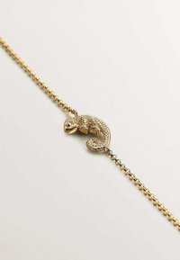 Pulsera de oro con un colgante en forma de camaleón, que presenta escamas texturizadas y una cola enroscada, montada sobre una cadena de eslabones.