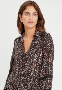 Chemise noire à manches longues avec un motif à speckles multicolores. Présente un col et un décolleté en V à boutons, avec un tissu texturé et des accents de couture délicats.