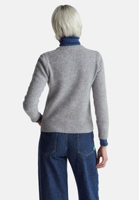 Světlounce šedý pletený svetr s žebrovaným lemem a manžetami, doplněný tmavě modrými širokými džínovými kalhotami. Hladká textura, ležérní design.